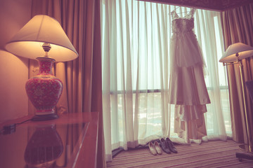 wedding dress hanging on luster at hotel room 	