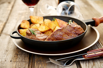 Beef steak in a pan with baked potatoes and red wine