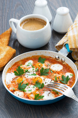 fried quail eggs in tomato sauce with toasts in a frying pan
