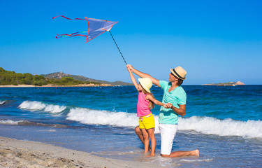 Happy father and little girl playing with kite on summer beach