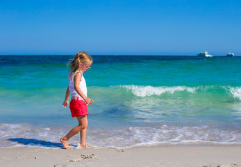 Fototapeta na wymiar Adorable little girl playing in shallow water at white beach