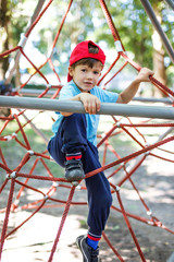 Little boy in cap climb on jungle gym