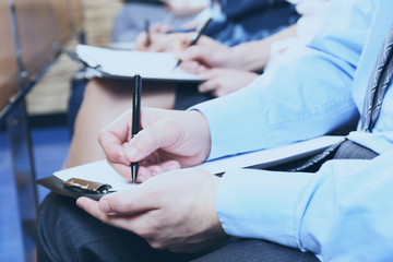 Hands holding pens and making notes at conference