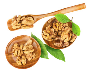 Handful of walnuts in wooden bowls, scoop and green leaves.
