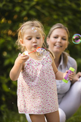 Mutter und Tochter blasen Seifenblasen im Garten
