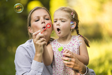 Mutter und Tochter blasen Seifenblasen im Garten