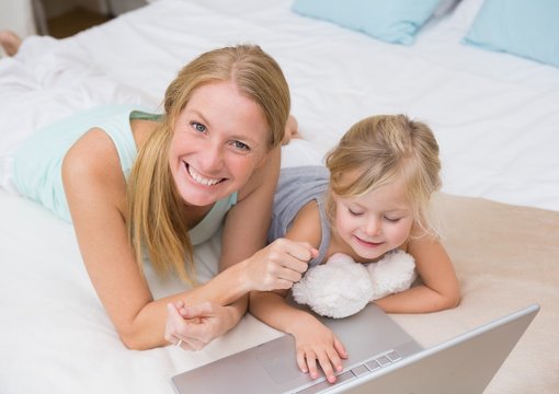 Cute little girl and mother on bed using laptop