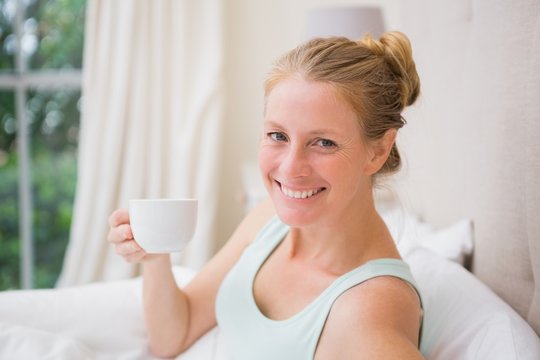 Happy blonde drinking coffee in bed