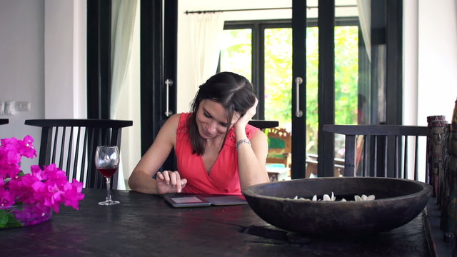 Young woman reading book on ebook reader by table at home