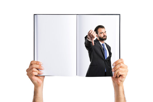 Young businessman with his thumb down printed on book