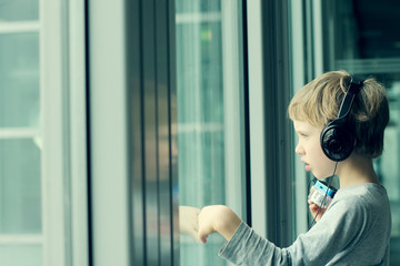 boy with headphones looking out the window at the airport - 70637464