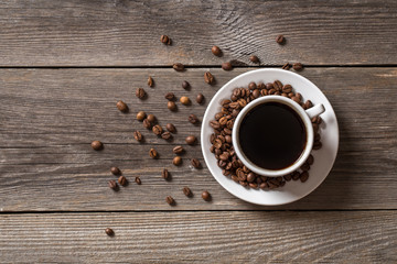 Coffee cup with roasted coffee beans on wooden table.