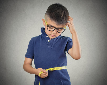 Child Measuring His Waistline Isolated On Grey Background 