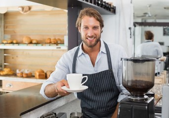 Handsome barista offering a cup of coffee to camera