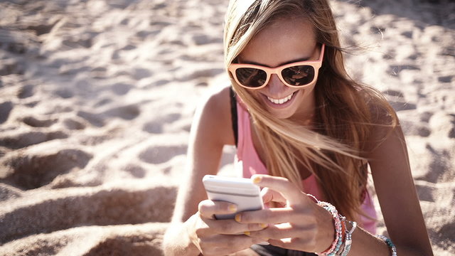 Girl sits on beach and messages on her phone