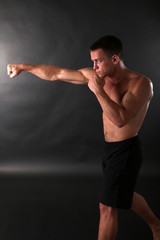 Fototapeta na wymiar Handsome young muscular sportsman boxing on dark background