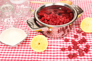 Red raspberries in metal pan, sugar, lemon and glass jars
