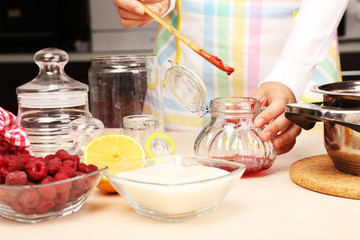 Woman cooking raspberry jam in kitchen