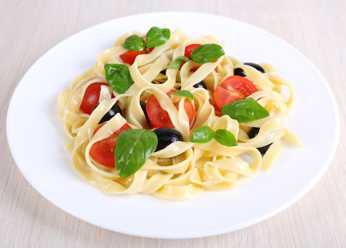 Spaghetti with tomatoes, basil and olives on plate on table