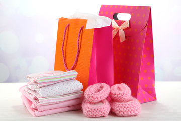 Baby clothes and gift bags on bright background
