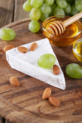 Brie cheese, honey in glass bowl, nuts and grapes