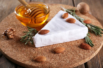 Brie cheese, honey in glass bowl and nuts on wooden background