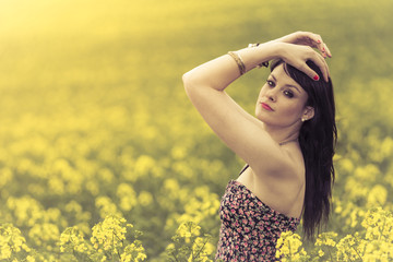 Beautiful woman in meadow of yellow flowers with hands up