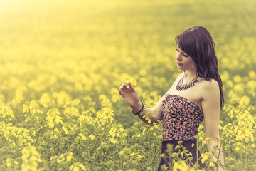 Beautiful woman in meadow of yellow flowers looking at flower