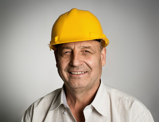 Smiling mature engineer or builder in yellow hardhat