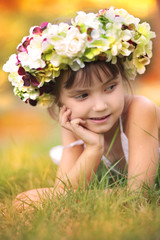 Obraz na płótnie Canvas Little girl in autumn wreath of flowers lying on the grass