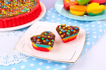 Delicious rainbow cakes on plates, on color wooden background