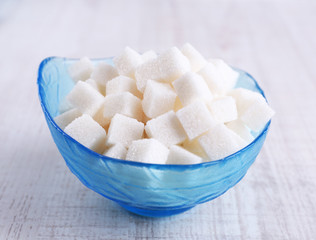 Refined sugar in color bowl on wooden background