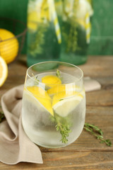 Tasty cool beverage with lemon and thyme, on wooden background
