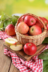 Sweet apples in wicker basket on table on bright background