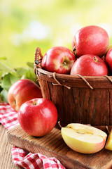 Sweet apples in wooden basket on table on bright background