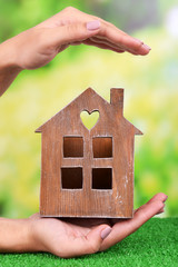 Woman hand holding small house on grass on bright background