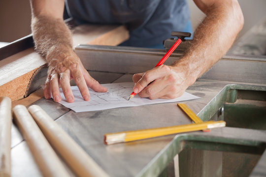 Carpenter Working On Blueprint At Tablesaw