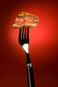 Piece Of A Grilled Steak On A Fork Isolated On Red