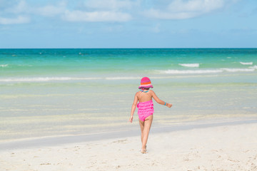 little girl in swimsuit walking on white sand beach near ocean