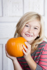 child holding small pumpkin up by her face