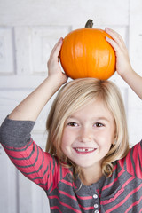 child holding small pumpkin on her head