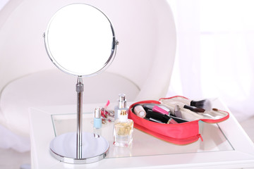 Cosmetic bag and mirror on table on light background