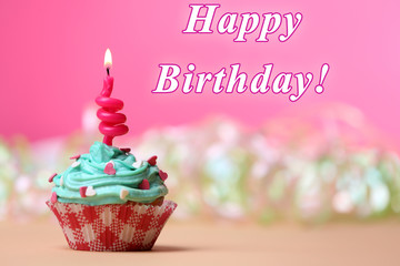 Delicious birthday cupcake on table on pink background