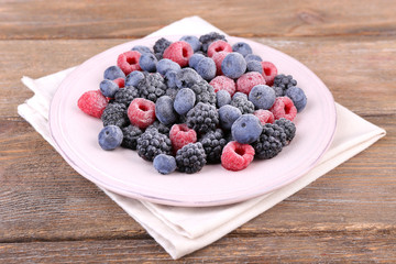 Iced berries on plate, on wooden background