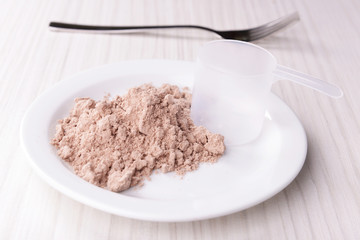 Whey protein powder on plate with scoop on wooden background