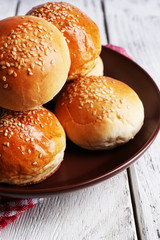 Tasty buns with sesame on plate, on color wooden background