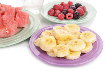 Sliced fruits and berries on plate with glass of water close up