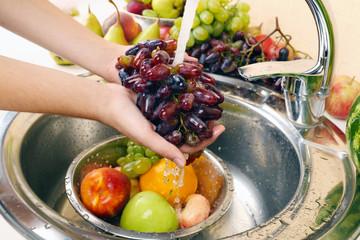 Woman's hands washing grapes and other fruits in colander in