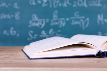 Book on wooden table on blackboard background