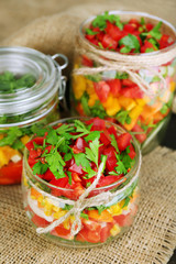 Vegetable salad in glass jars, on wooden background